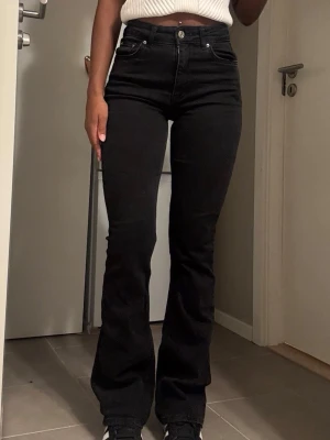 Svarta bootcut jeans med hög midja - Säljer ett par svarta bootcut jeans med hög midja och klassisk femficksmodell. Jeansen har en snygg, figurnära passform upptill och lätt utsvängda ben. Materialet är stretchigt denim som sitter bekvämt hela dagen. Perfekta till sneakers eller boots.