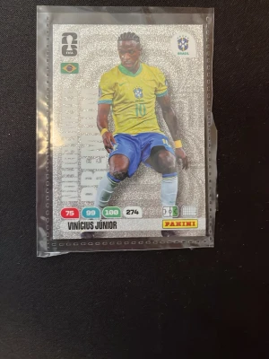 Panini Adrenalyn FIFA VM 2026 kort - Samlarbild från Panini Adrenalyn FIFA World Cup 2026 med brasiliansk spelare. Kortet har glittrig silverbakgrund, spelarnamn och landslagsfärger i gult, blått och grönt. Perfekt för dig som gillar fotboll och samlarkort.