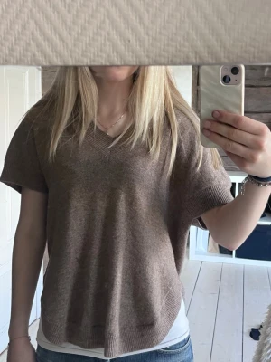 Stickad tröja från WERA - Säljer en brun stickad t-shirt med v-ringning och korta ärmar. Tröjan har en avslappnad passform och ribbade kanter vid ärmslut och nederkant. inga tecken på användning. Lyxigt material, 100%ull 