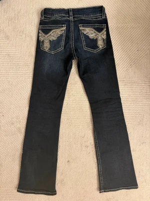 Mörkblå bootcut jeans med brodyr - Supersnygga mörkblå bootcut jeans med fina fickor från Gina Tricot Young!!Jeansen har låg midja och detaljerade fickor med coolt mönster i beige och silver. De är i väldigt bra skick och passar till många stilar och kläder. Säljer endast pågrund av att de blivit för små. Förlåt om bilderna inte är så bra tagna, kan skicka fler om någon vill se jeansen i bättre ljus eller vinkel t.ex. Pris kan diskuteras. 💗💗