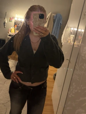 Mörkgrå cropped kofta med knappar - Snygg mörkgrå kofta med knäppning framtill och croppad passform. Långa ärmar och enkel design som passar till mycket. Perfekt att slänga över en topp eller linne för en avslappnad look.