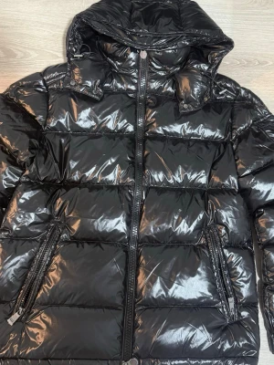 Moncler Maya - Säljer en svart Moncler Maya med huva och två dragkedjeförsedda fickor framtill. Jackan är i jättebra skick, har använt bara några gånger. Jackan har klassisk Moncler-logga på ärmen och quiltad design. Perfekt för kalla vinterdagar och riktigt snygg streetstil.                                                              Storlek S, pris kan diskuteras vid snabb affär.           Skickar snabbt✅