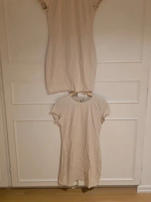 Beige kort t-shirtklänning - Enkel och stilren beige t-shirtklänning med rund hals och korta ärmar. Klänningen har en rak passform och är gjord i mjukt bomullsmaterial. Har två av dessa klänningar, så säljer 1 i vardera annons. Från Biancas kollektion med Nelly. Aldrig använd 