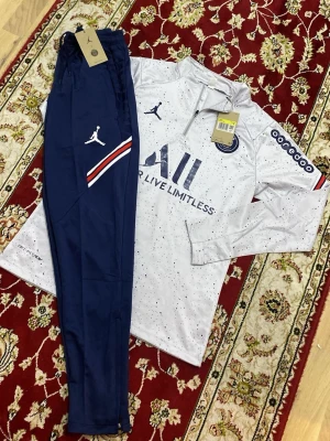PSG träningsset Jordan x Nike S - Säljer ett PSG träningsset från Jordan x Nike. Setet består av en vit långärmad tröja med blå detaljer, halv dragkedja och små blå prickar samt blå byxor med vita och röda detaljer. Perfekt för fotbollsträning eller sportiga dagar.