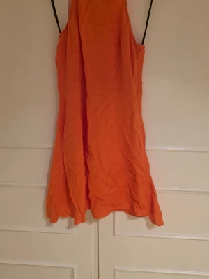 Corall färgad klänning - Corall färgad klänning, en kortare modell med korsliknande på ryggen och väldigt flowigt tyg