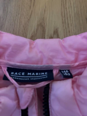 Ljusrosa pufferjacka Race Marine  - Säljer en ljusrosa pufferjacka från Race Marine med quiltat mönster och svarta dragkedjor. Jackan har rund krage, två fickor framtill och detaljer med Race Marine-tryck på muddar och nederkant. Perfekt för kalla dagar och riktigt snygg till vardags.