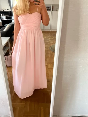 Rosa balklänning  - En superfin rosa balklänning. Den funkar både med och utan band ifall man skulle vilja ta av dom. Storlek S. Midjemått: 77cm. Bystmått: 82cm. Längd:126 cm. Dragkedjans längd: 43cm💕 klänningen är för liten för mig därav att dragkedjan inte är uppdragen helt.