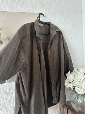 Brun/mörkgrön oversized manchesterskjorta - Säljer en brun/mörkgrön oversized skjorta i mjuk manchester med klassisk krage och knappar framtill. Perfekt för en avslappnad och trendig look. Skjortan har långa ärmar och en loose passform som ger en chill vibe.
