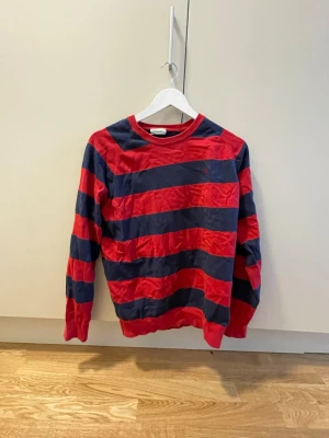 Randig röd och marinblå stickad tröja - Snygg stickad tröja med breda röda och marinblå ränder. Tröjan har rund halsringning och långa ärmar. Perfekt för dig som gillar en sportig och avslappnad stil.