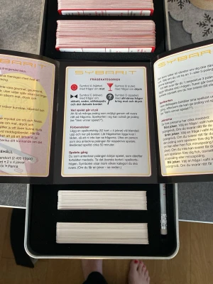 Sällskapsspelet Sybarit i plåtlåda - Sybarit är ett frågespel om mat och dryck med 400 frågor. Spelet kommer i en silverfärgad plåtlåda med präglat motiv av bestick och korkskruv. Innehåller spelkort, regler och penna. Perfekt för dig som gillar quiz och vill utmana vänner på kunskap om mat och dryck.