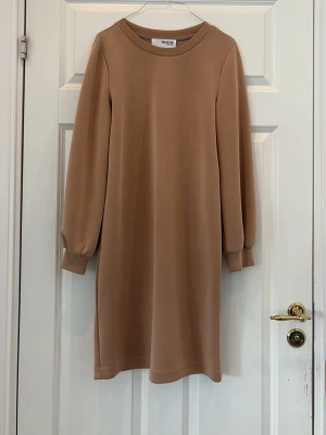 Beige långärmad klänning Selected Femme - En stilren beige klänning från Selected Femme med lång ärm och rund halsringning. Klänningen har en rak passform och är tillverkad i ett mjukt material som känns skönt mot huden. Perfekt för dig som gillar enkel och modern stil. I stretchigt material 