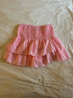 Rosa volangkjol från Meet me There - Supersöt rosa kortkjol med volanger och små vita blommor, från Meet me There. Nyskick då den bara är använd en gång 💓 Storlek S/M.