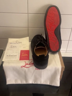 Svarta loafers från Christian Louboutin - Säljer ett par svarta loafers från Christian Louboutin med den ikoniska röda sulan och diskret snörning. Skorna har en stilren design i mocka och kommer med originalpåse och certifikat. Perfekta för dig som vill ha något exklusivt och trendigt.