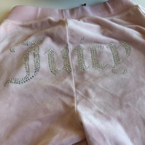 Juicy Couture - Snygga rosa mjukisbyxor från Juicy Couture med glittrande stenar som bildar texten 'Juicy' på baksidan. Byxorna har en bekväm passform och är perfekta för en avslappnad stil.