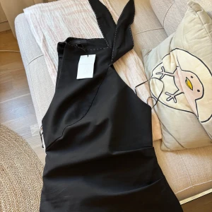 Svart ärmlös omlottopp från Zara - Snygg svart omlottopp från Zara med breda axelband och asymmetrisk skärning. Toppen är ärmlös och har en stilren look som passar perfekt till jeans eller kjol. Materialet känns mjukt och har en lätt stretch. Priset är diskuterbart vid snabb affär.