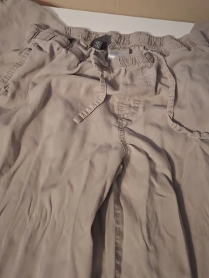Beige linnebyxor från H&M med dragsko - Snygga beige linnebyxor från H&M med avslappnad passform och elastisk midja med dragsko. Byxorna har sidofickor och är tillverkade i ett lätt och luftigt linnematerial, perfekta för en chill och stilren look.
