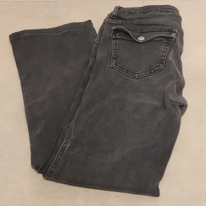 Svarta raka jeans med fickdetalj - Säljer ett par svarta jeans med rak passform och snygg fickdetalj bak med lock och knapp. Jeansen har klassisk femficksdesign.  Perfekta till en avslappnad streetstil eller att matcha med en hoodie.