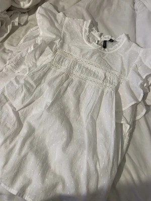 Vit blus med spets från Vero Moda - Söt vit blus från Vero Moda med voluminösa korta ärmar och fina spetsdetaljer över bröstet. Blusen har diskret prickstruktur i tyget och volang vid halsringningen. Perfekt för en romantisk och trendig look. Aldrig använd! nypris 300 säljer för 200 pris kan diskuteras