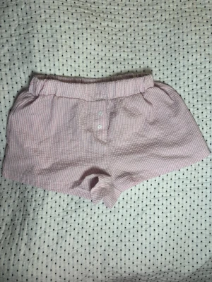 Rosa och vita rutiga shorts - Säljer ett par söta rosa och vita rutiga shorts med elastisk midja och knappdetaljer framtill och har en avslappnad passform även lågmidja. 