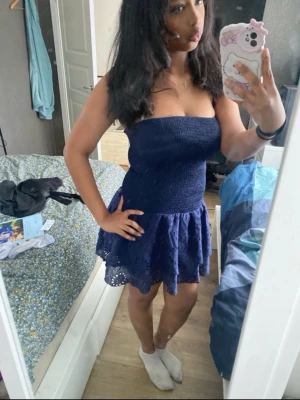 Mörkblå axelbandslös kortklänning - Söt mörkblå axelbandslös kortklänning med smockad överdel och volangig kjol med broderade detaljer. Perfekt för varma dagar och enkel att styla med accessoarer.