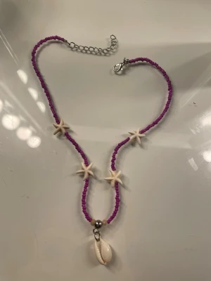 Lila pärlhalsband med snäckor - Säljer ett fint lila strand inspirerat halsband. Köpt i Brasilien. Mycket gott skick då det nästan aldrig använts. Kontakta om du är intresserad eller har frågor!