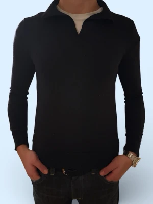 Stickad merino ull tröja med krage - Stilren svart långärmad tröja med klassisk krage och v-ringad öppning framtill. Tröjan har en smal passform och är tillverkad i merino ull ett mjukt, stretchigt material som sitter snyggt på kroppen. Perfekt för dig som gillar en enkel men trendig look.