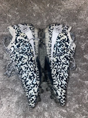 Under Armour Magnetico fotbollsskor - Säljer ett par Under Armour Magnetico fotbollsskor med svartvitt pixelmönster. Skorna har snörning, låg profil och är tillverkade i syntetmaterial för bra passform och grepp på planen. Perfekta för dig som vill sticka ut på fotbollsplanen.