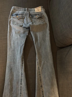 True religion  - Säljer ett par ljusblå bootcut jeans från True Religion med klassiska fickdetaljer bak och utsvängda ben. Jeansen har synliga sömmar och en ikonisk patch bak i midjan. Perfekta för dig som gillar en avslappnad och trendig look. Jeansen är endast använda ett par gånger då jag säljer pga fel storlek. Jeansen är i storlek 26 och i färgen peak spot!