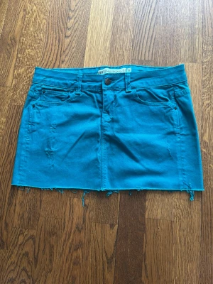 Turkos jeanskjol med rå kant - Snygg turkos jeanskjol från Only med fem fickor, slitna detaljer och rå, fransig nederkant. Kjolen har klassisk knapp- och dragkedjestängning samt bälteshällor. Perfekt för en trendig och avslappnad look. Skriv för fler bilder!