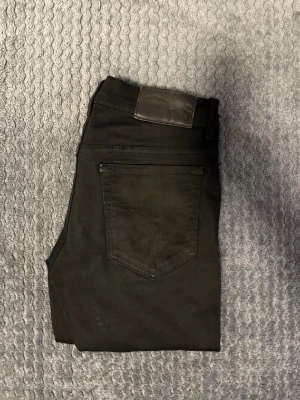 Tiger of Sweden  - Snygga svarta jeans med klassisk femficksdesign och en stilren skinnpatch i midjan. Jeansen har raka ben och är perfekta för en clean och modern look. Passar till det mesta och är lätta att matcha med olika outfits.