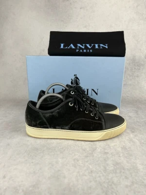Svarta sneakers från Lanvin i mocka - Snygga svarta sneakers från Lanvin i mjuk mocka med detaljer i läder på tån och snörning. Skorna har en vit sula med retrovibbar och metallfärgade öljetter. Perfekta för dig som gillar stilrena och exklusiva sneakers.