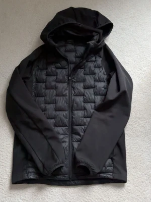 Everest jacka - Säljer en svart pufferjacka med huva och dragkedja framtill. Jackan har quiltad front och släta ärmar, samt elastiska muddar vid ärmsluten. Perfekt för kalla dagar och enkel att matcha med olika outfits.