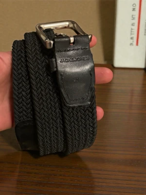  flätat bälte från Jack & Jones - Snyggt svart flätat bälte från Jack & Jones med silverfärgat spänne och detaljer i skinn. Perfekt accessoar för att lyfta din outfit och passar till både jeans och chinos.