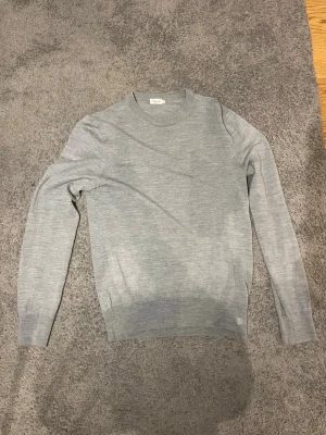Ljusgrå stickad tröja Filippa K - Snygg ljusgrå stickad tröja från Filippa K i tunn ullmix. Klassisk rund halsringning och långa ärmar. Perfekt basplagg med ribbade muddar vid ärmslut och nederkant. Enkel och stilren design som passar till det mesta.