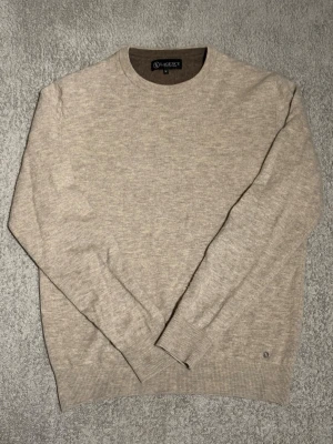 Stickad tröja LAGENCY - Beige stickad tröja från LAGENCY med rund halsringning och ribbade muddar vid ärmslut och nederkant. Tröjan har en klassisk och stilren design, perfekt för lager-på-lager och enkel att matcha med olika outfits.