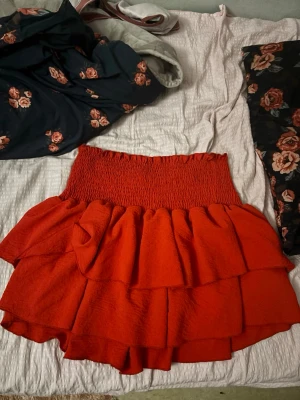 Röd volangkjol med smock - Snygg röd kortkjol med bred smock i midjan och dubbla volanglager. Passar till både sneakers och boots.