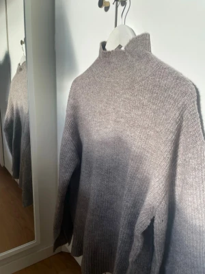 Grå stickad polotröja i ullmix - Säljer en stilren grå stickad polotröja i mjuk ullmix. Tröjan har hög krage och avslappnad passform, perfekt för kyliga dagar. Enkel att matcha med jeans eller kjol för en trendig look.