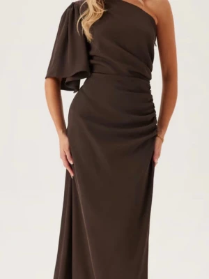 Brun oneshoulder långklänning - Snygg brun långklänning med oneshoulder-design och draperad detalj i midjan. Klänningen har en vid ärm på ena sidan och är ärmlös på andra, vilket ger en cool och elegant look. Perfekt för dig som vill sticka ut. Helt oanvänd och slutsåld på hemsidan! 