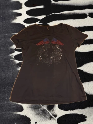 Svart t-shirt med tryck  - Cool svart t-shirt med korta ärmar och tryck framtill med två amerikanska flaggor och glittriga detaljer. använd få gånger