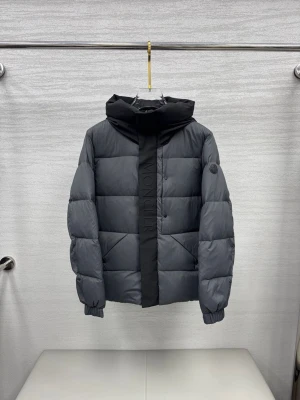Moncler Madeira - Snygg svart dunjacka från Moncler med stor huva och breda, quiltade paneler. Jackan har Moncler-logga på ärmen och diskret Moncler-tryck längs dragkedjan. Perfekt för kalla vinterdagar och riktigt stilren look.
