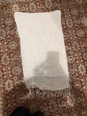 Vit sjal med fransar - Enkel och stilren vit sjal i tunt tyg med fransar längs kanterna. Rektangulär form och lätt material som känns luftigt.