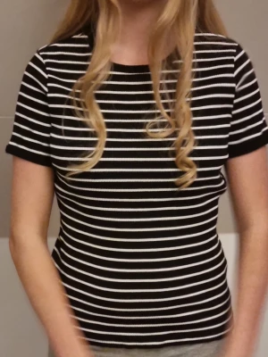 Svartvit randig topp med kort ärm - Snygg svart topp med vita horisontella ränder och rund hals. Modellen är kortärmad och har en figurnära passform. Perfekt till jeans eller kjol för en enkel men trendig look. Aldrig använd pga för stor