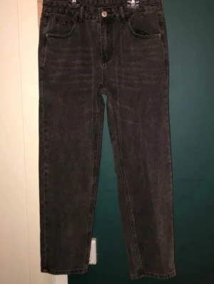 Svarta raka jeans med hög midja - Säljer ett par svarta raka jeans med hög midja och klassisk femficksmodell. Jeansen har en knappgylf och är tillverkade i ett kraftigt denimtyg. Perfekta för dig som gillar en avslappnad och tidlös stil.