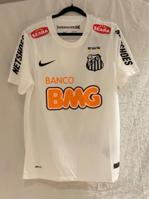 Santos FC Neymar JR 11 - Säljer en vit Santos FC matchtröja från säsongen 11/12. Tröjan har klubbmärke, sponsorloggor och Nike Swoosh på bröstet. Tillverkad i lätt och ventilerande material, perfekt för fotboll eller träning.