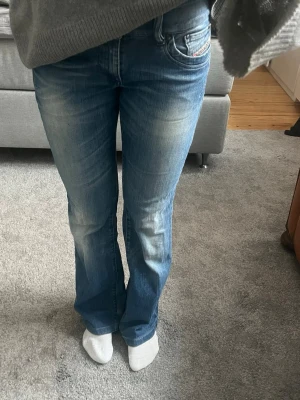 Blå bootcut jeans från Diesel - Säljer ett par blå bootcut jeans från Diesel med snygga slitningar och klassiska fem fickor. Jeansen har en ljus tvätt och subtila detaljer vid fickorna. Perfekta för en avslappnad och trendig look. Storlek w 28 L 34