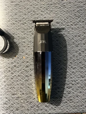 JRL hårtrimmer svart/guld - Elektrisk hårtrimmer från JRL med svart och guldfärgat handtag och metalliskt bladhus. Trimmern har ett T-format skärhuvud i metall och en stilren, modern design. Perfekt för att fixa detaljerade frisyrer och linjer.