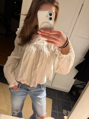 Vit blus med volanger och prickar - Säljer en vit blus med diskreta små prickar av guld och volangdetaljer vid axlarna. Blusen har lång ärm med resår och rynkade detaljer, samt en lös och luftig passform. Perfekt för dig som gillar romantisk och trendig stil. Pris kan diskuteras vid snabb affär!💕