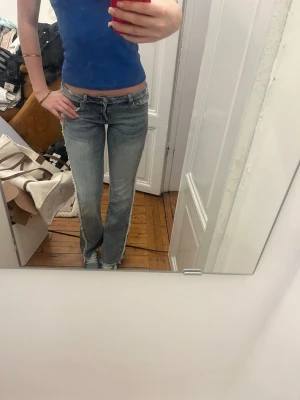 Ljusblå low waist bootcut jeans - Säljer ett par ljusblå jeans med låg midja och bootcut-modell. Jeansen har klassisk femficksdesign och slitningar vid bensluten för en avslappnad look. Perfekta för dig som gillar 00-talsstil och vill ha ett par riktigt snygga jeans i garderoben.