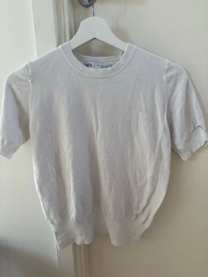 Vit kortärmad topp från Zara - En stilren vit topp från Zara med rund halsringning och korta ärmar. Toppen har en enkel och klassisk design, perfekt att matcha med olika outfits. Materialet känns mjukt och bekvämt mot huden🤍