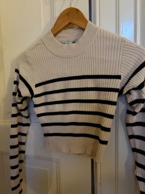 Stickad randig croptopp - Säljer en stickad croptopp från lager 157. Den har beige/svarta ränder. Modellen är ribbad i stretch med rund krage. Tröjan är i storlek M men är liten i storlek, närmare storlek S. Den är i nyskick men utan prislapp/förpackning. 